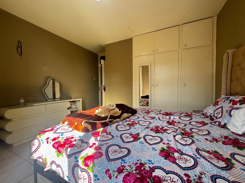 A bedroom featuring built-in cupboards with a mirrored panel and tiled flooring, offering a functional space with potential for cosmetic updates.