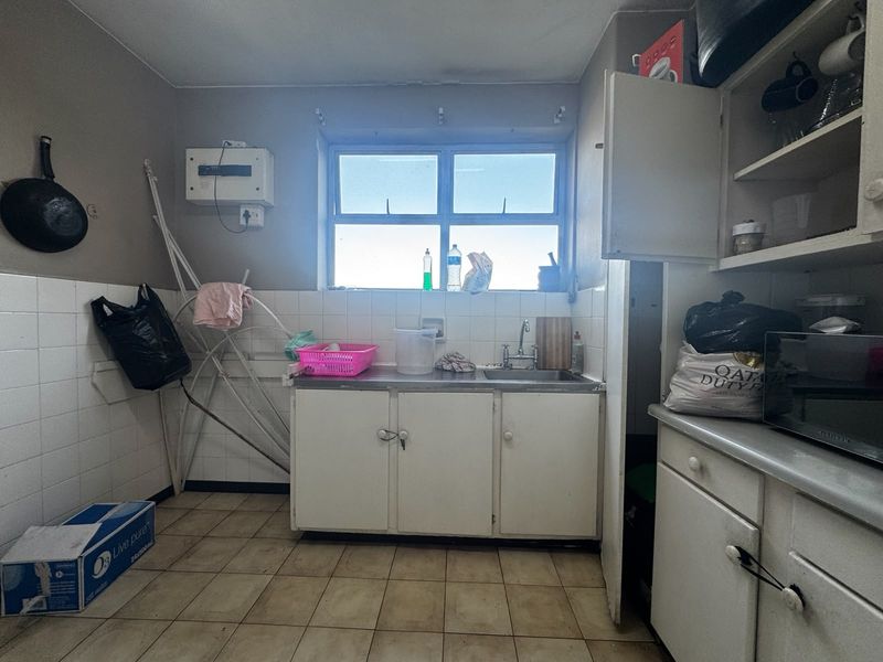 A functional kitchen area featuring built-in cabinetry, a stainless steel sink, and tiled splashbacks, offering potential for modernization and cosmetic updates.