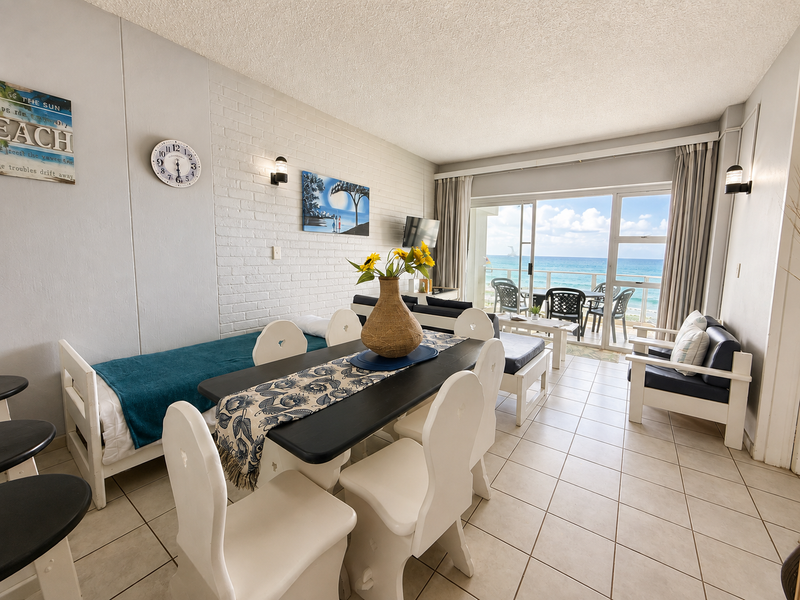 Open-plan living and dining area featuring ceramic tile flooring, an exposed brick feature wall, and large sliding doors opening to a balcony with ocean views.