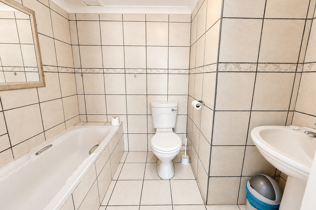 A functional bathroom featuring a bathtub, pedestal basin, and toilet with neutral floor-to-ceiling wall tiles.