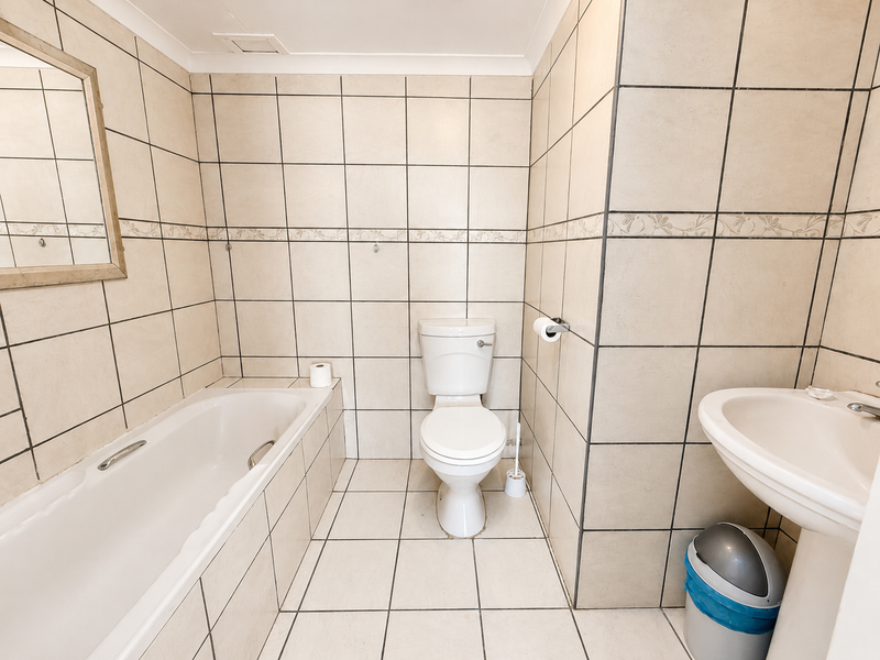 A functional bathroom featuring a bathtub, pedestal basin, and toilet with neutral floor-to-ceiling wall tiles.