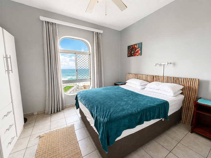 A bedroom featuring tiled flooring, a ceiling fan, and an arched window offering ocean views.