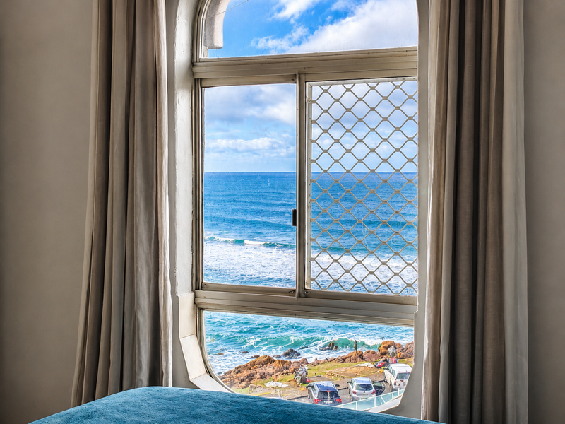 A bedroom featuring an arched window with a security grille, offering a direct view of the ocean and coastline.