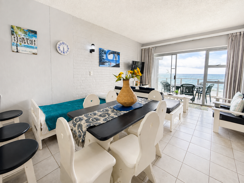 Open-plan living and dining area featuring painted brick walls, ceramic tile flooring, and large sliding glass doors leading to a balcony with ocean views.