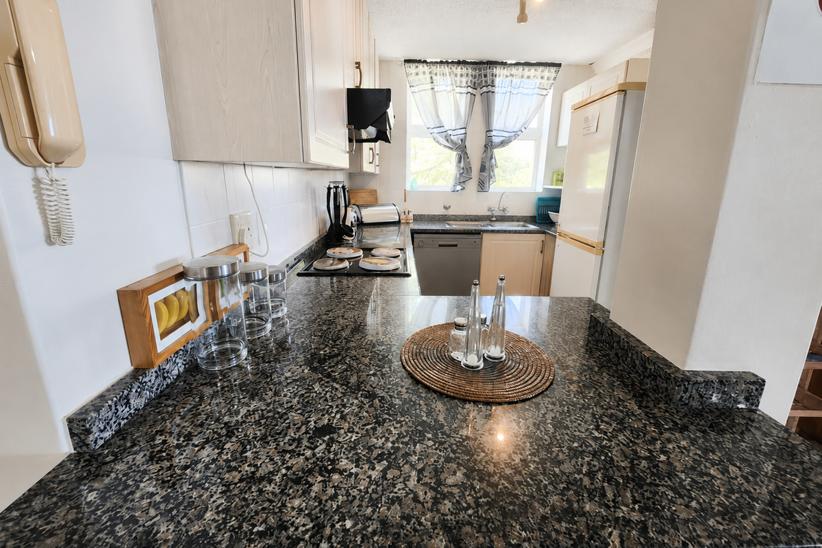 A functional kitchen featuring granite countertops, built-in cabinetry, an electric hob, and an integrated sink, offering a practical layout for daily meal preparation.