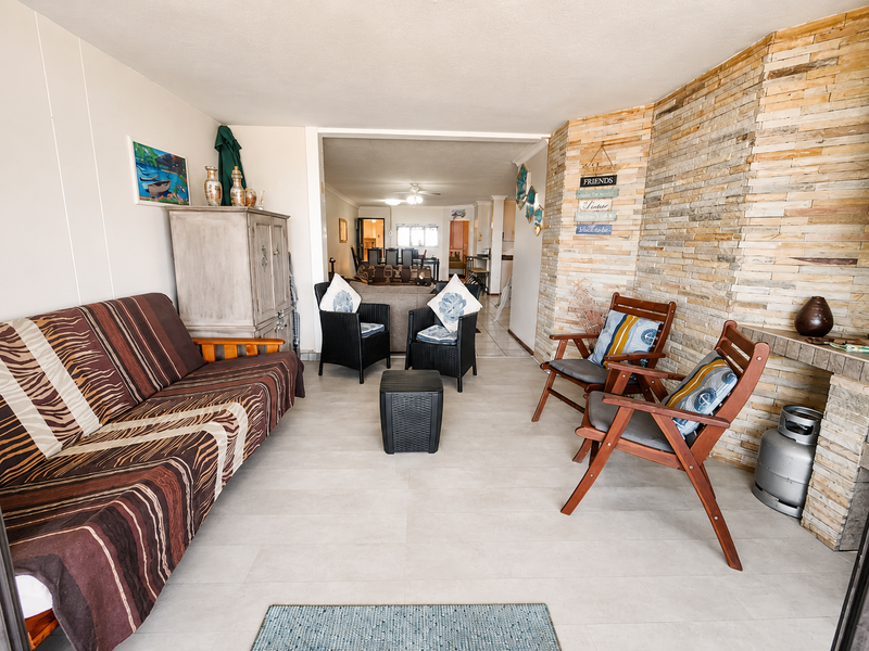 A spacious covered patio featuring a decorative stone-clad wall, built-in fireplace, and neutral tiled flooring, offering a comfortable transition to the interior living area.