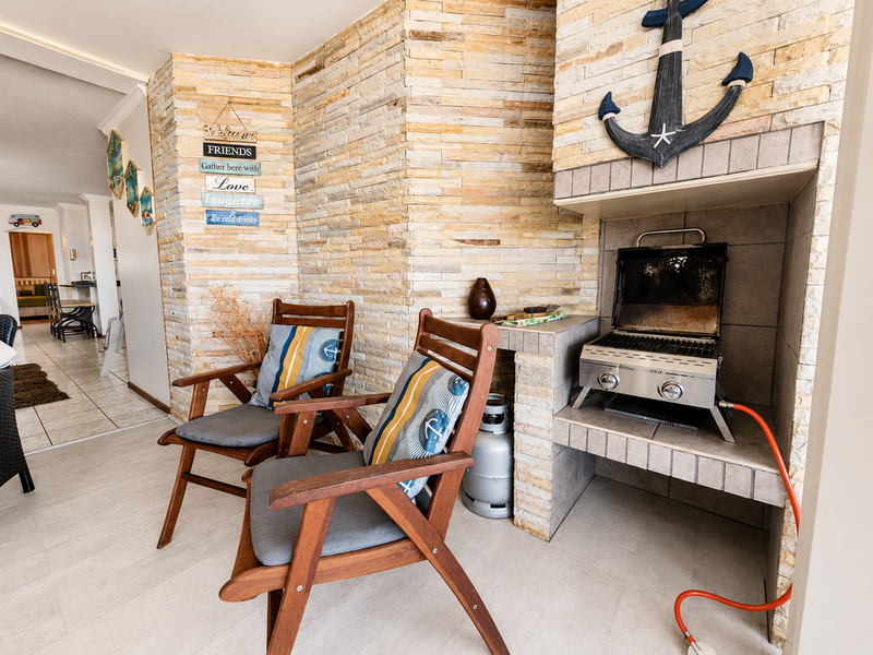 Covered patio area featuring a built-in stone fireplace and tiled flooring, providing a functional space for outdoor cooking and relaxation.