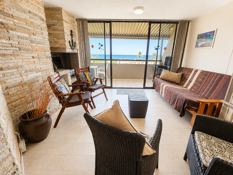 Open-plan living area featuring a stone-clad fireplace, built-in braai, and large sliding glass doors opening onto a balcony with ocean views.