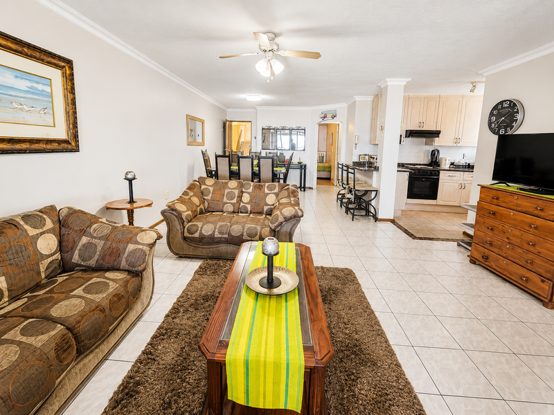 Open-plan living and dining area featuring tiled floors, a ceiling fan, and a functional kitchen with built-in cabinetry and appliances.