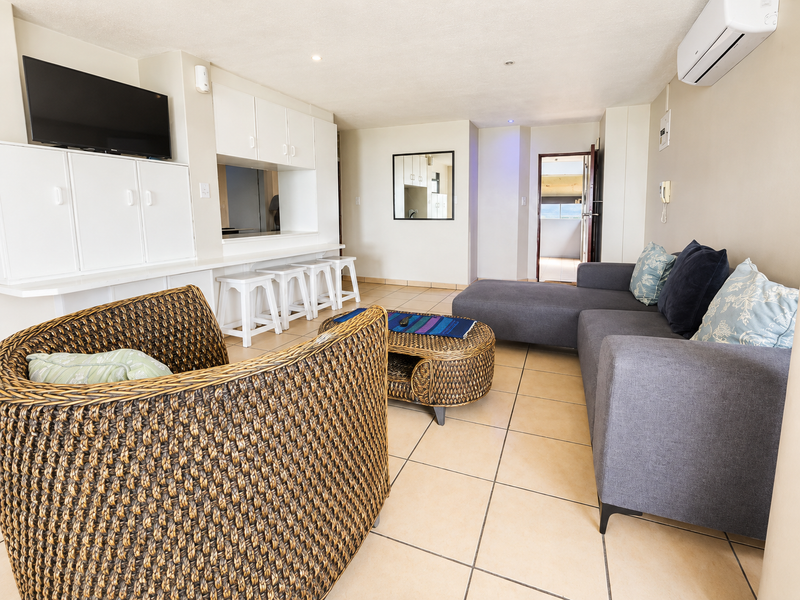 Open-plan living area featuring tiled flooring, built-in cabinetry with a breakfast bar, and a wall-mounted air conditioning unit.
