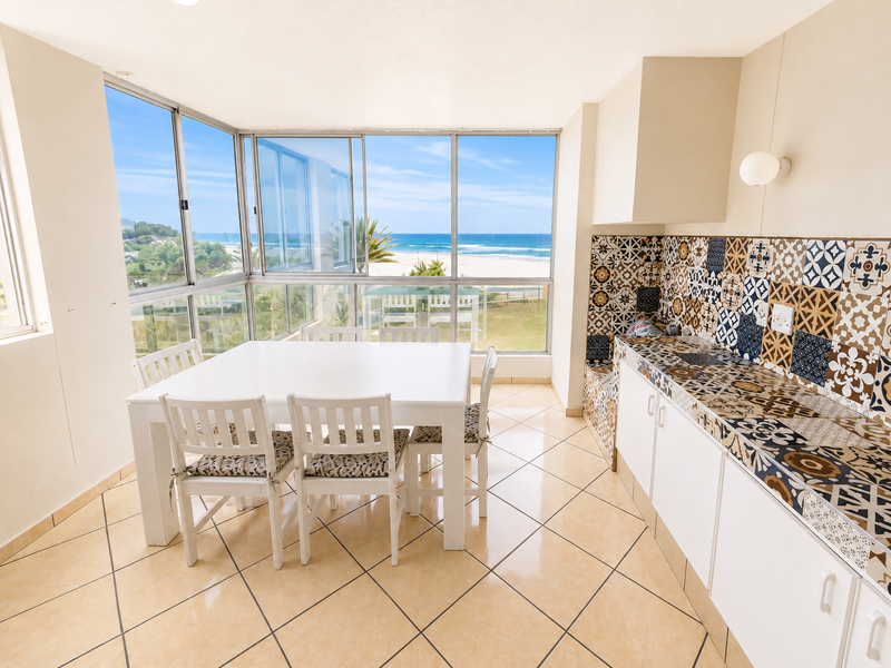 Open-plan dining and kitchen area featuring patterned tile backsplash, tiled floors, and expansive windows offering panoramic ocean views.