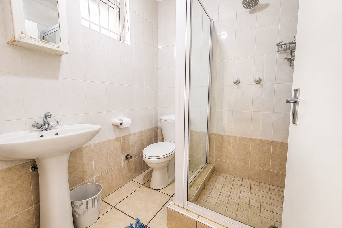 A functional bathroom featuring a pedestal basin, toilet, and a glass-enclosed shower with neutral wall and floor tiling.