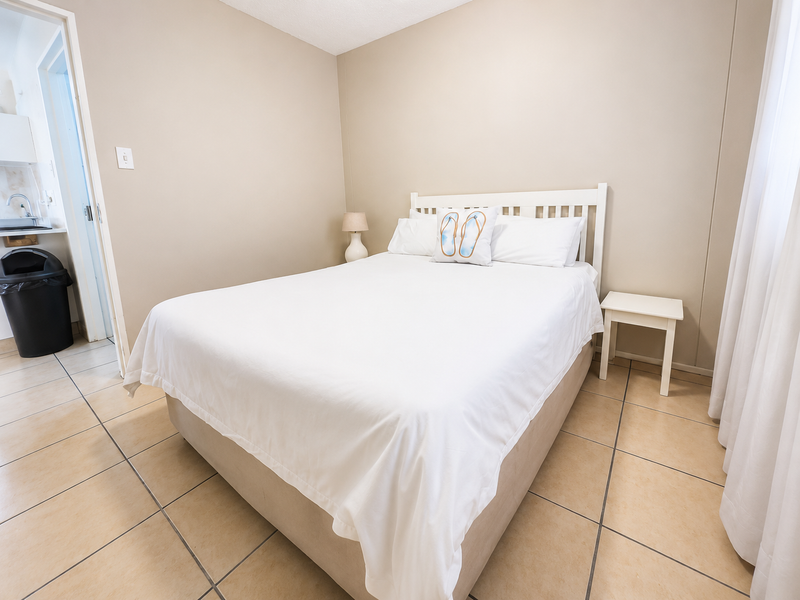 A simple bedroom featuring neutral wall tones and tiled flooring, with direct access to an adjacent utility or bathroom area.