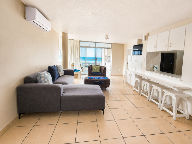 Open-plan living area featuring tiled floors, built-in cabinetry, a split-system air conditioner, and direct access to a balcony with ocean views.