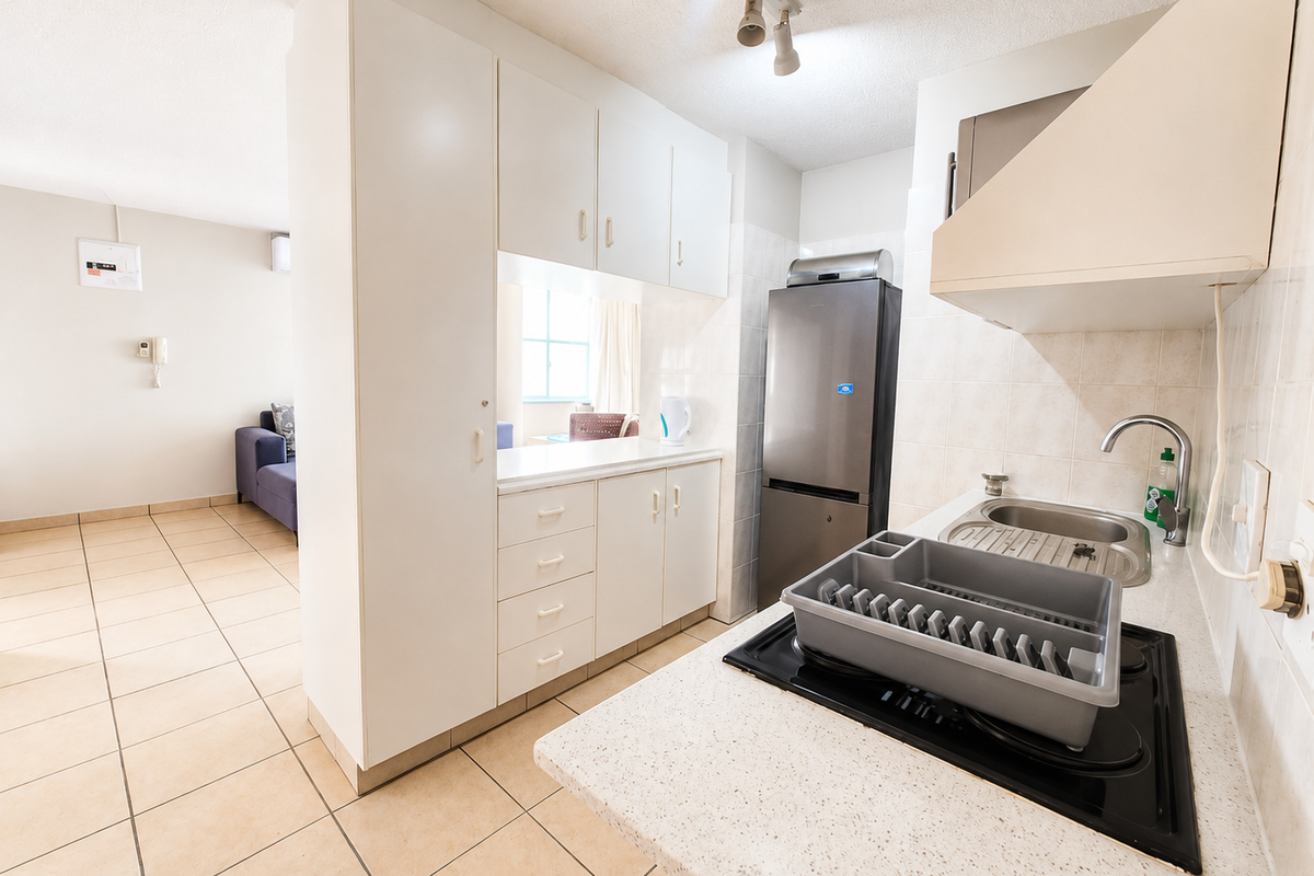 Compact kitchen featuring white built-in cabinetry, laminate countertops, an electric hob with extractor fan, and tiled finishes, opening into the adjacent living area.