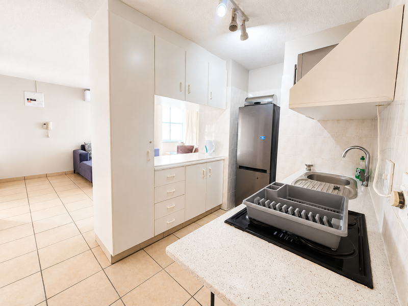 Compact kitchen featuring white built-in cabinetry, laminate countertops, an electric hob with extractor fan, and tiled finishes, opening into the adjacent living area.
