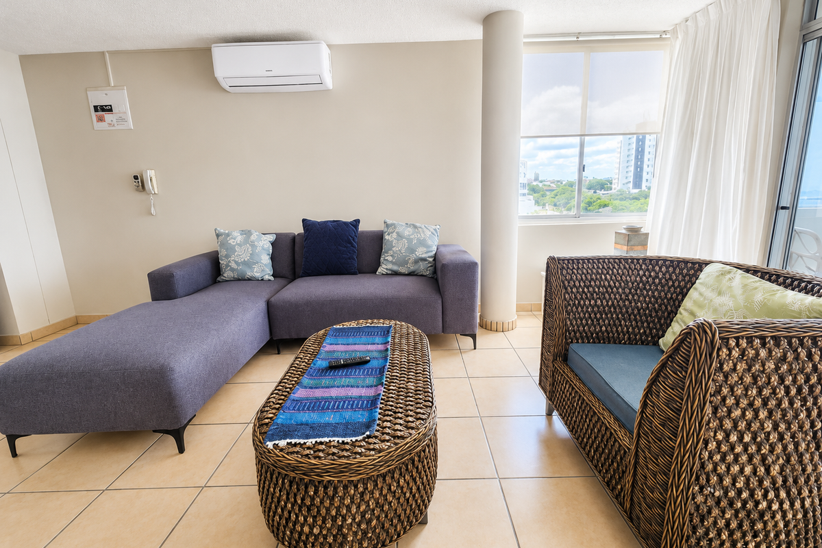 A bright living room featuring tiled flooring, a structural column, and a wall-mounted air conditioning unit with access to a balcony.