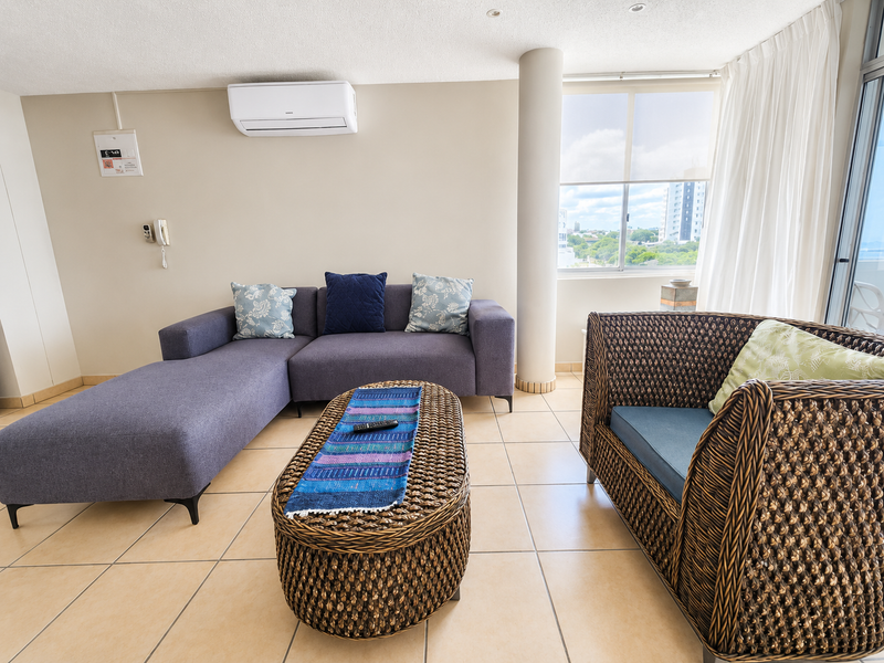 A bright living room featuring tiled flooring, a structural column, and a wall-mounted air conditioning unit with access to a balcony.