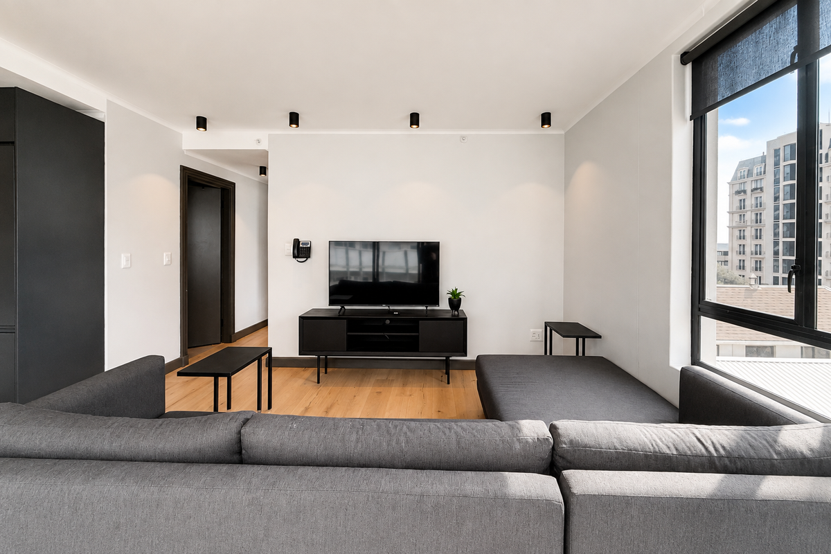 Modern living room featuring timber flooring, recessed ceiling spotlights, and large windows with black frames, offering a clean and contemporary aesthetic.