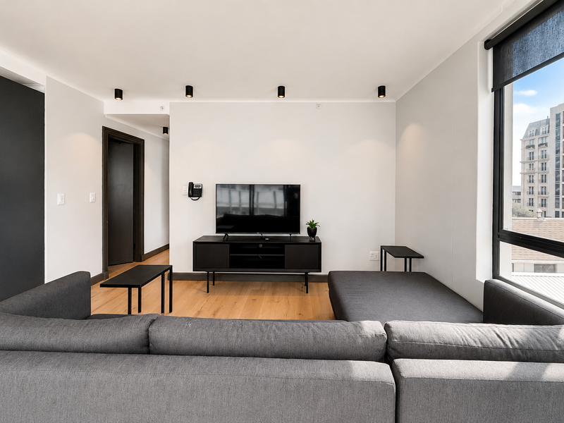 Modern living room featuring timber flooring, recessed ceiling spotlights, and large windows with black frames, offering a clean and contemporary aesthetic.