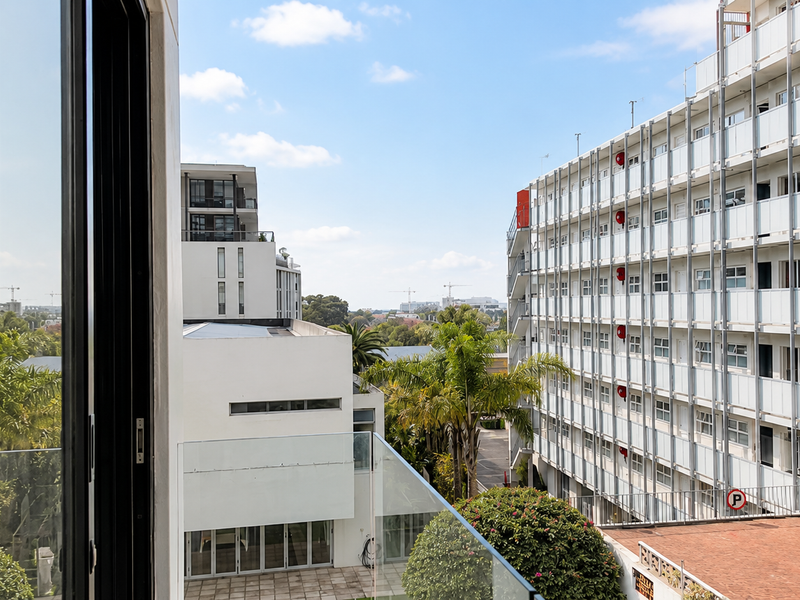 An elevated urban view from a balcony looking out over surrounding apartment buildings and landscaped grounds.