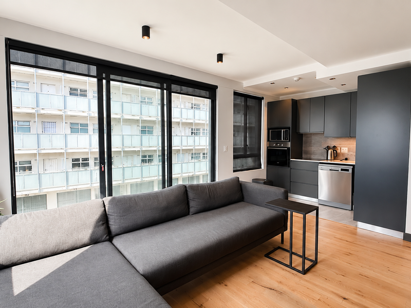 Modern open-plan living area featuring sleek dark cabinetry, integrated kitchen appliances, timber flooring, and large sliding glass doors providing ample natural light.