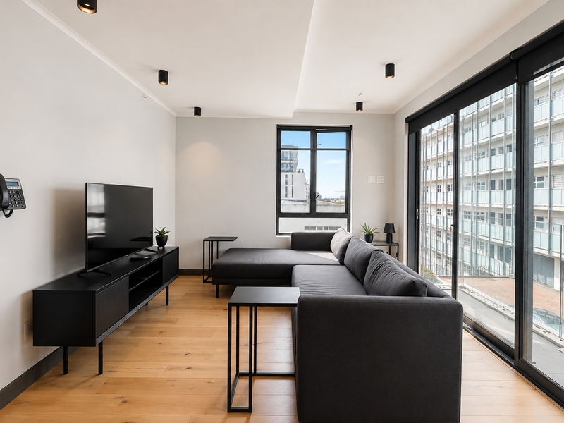 Modern living room featuring hardwood flooring, recessed lighting, and large sliding glass doors providing ample natural light and access to the balcony.