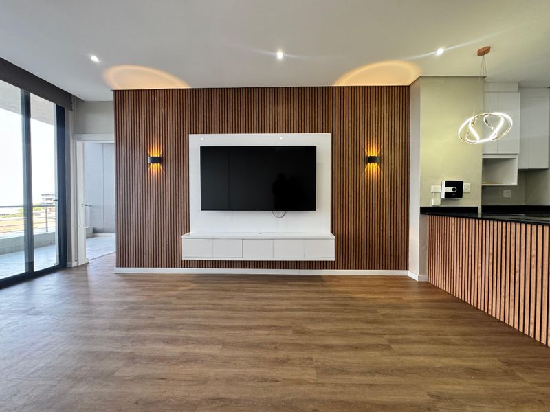 Modern open-plan living area featuring a stylish timber slat feature wall, built-in media console, and seamless access to the balcony.