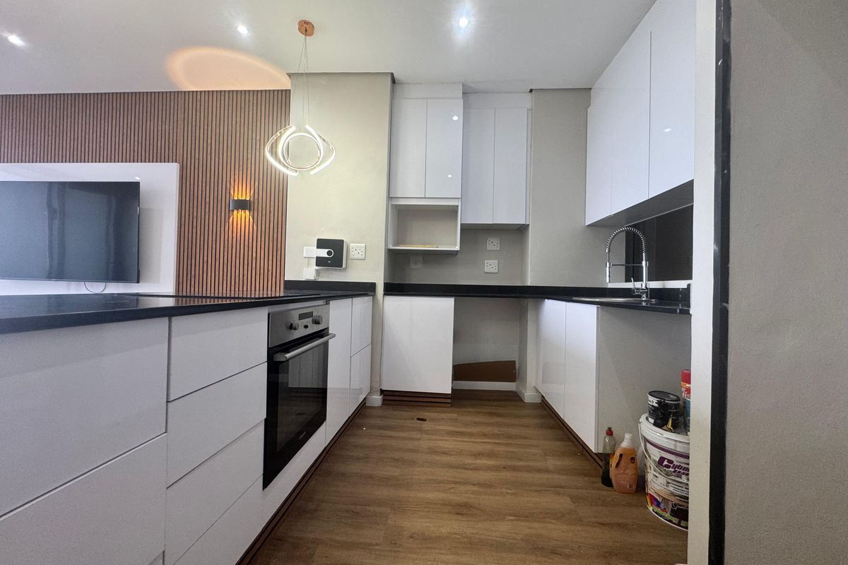 Modern kitchen featuring white gloss cabinetry, black granite countertops, built-in oven, and wood-look flooring, adjacent to a stylish slatted wood feature wall.