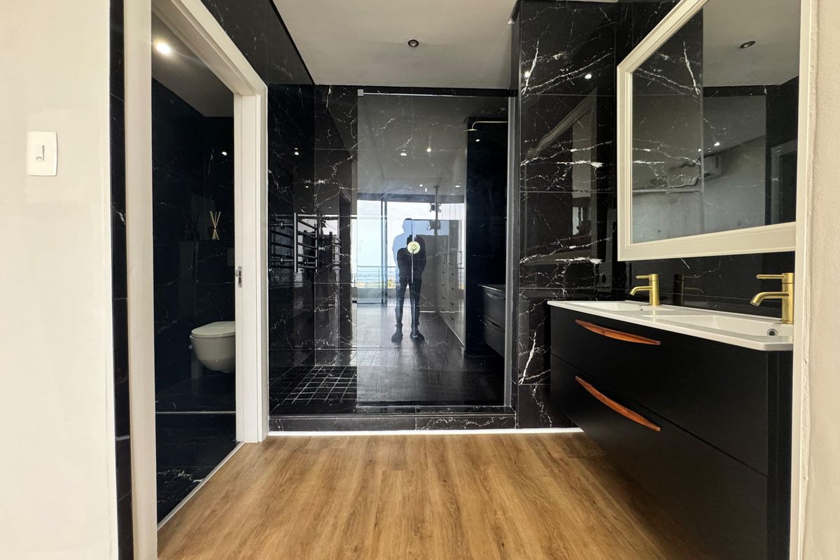 Modern bathroom featuring black marble-effect wall tiles, a sleek double vanity with gold-tone faucets, and a spacious walk-in shower.