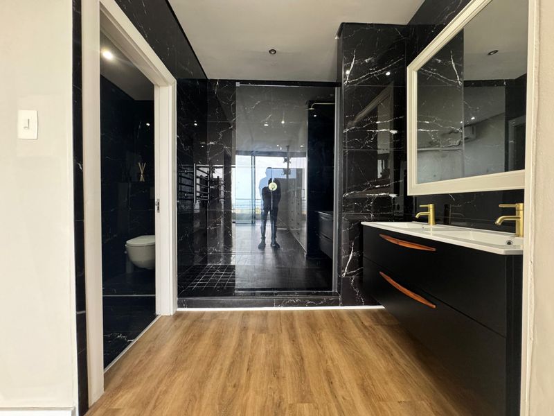Modern bathroom featuring black marble-effect wall tiles, a sleek double vanity with gold-tone faucets, and a spacious walk-in shower.