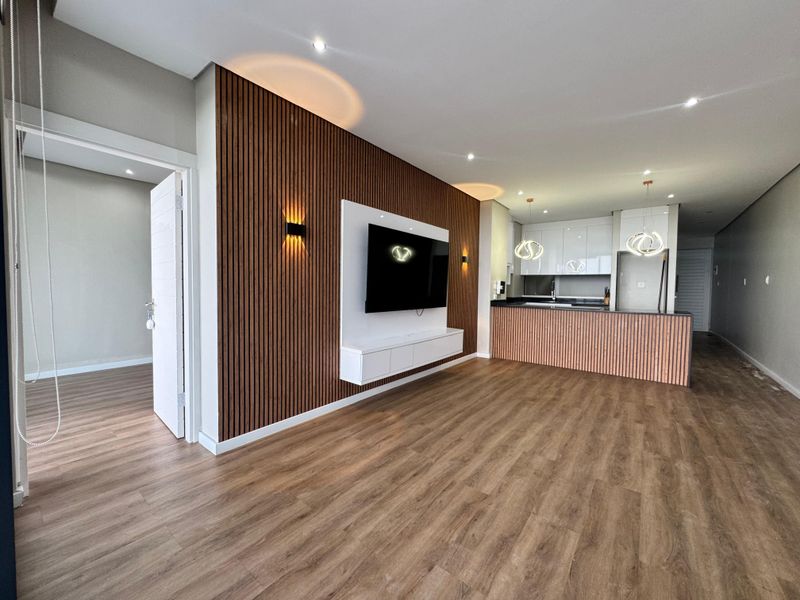 Modern open-plan living area featuring a stylish timber slat feature wall, laminate flooring, and a contemporary kitchen with gloss cabinetry and island.