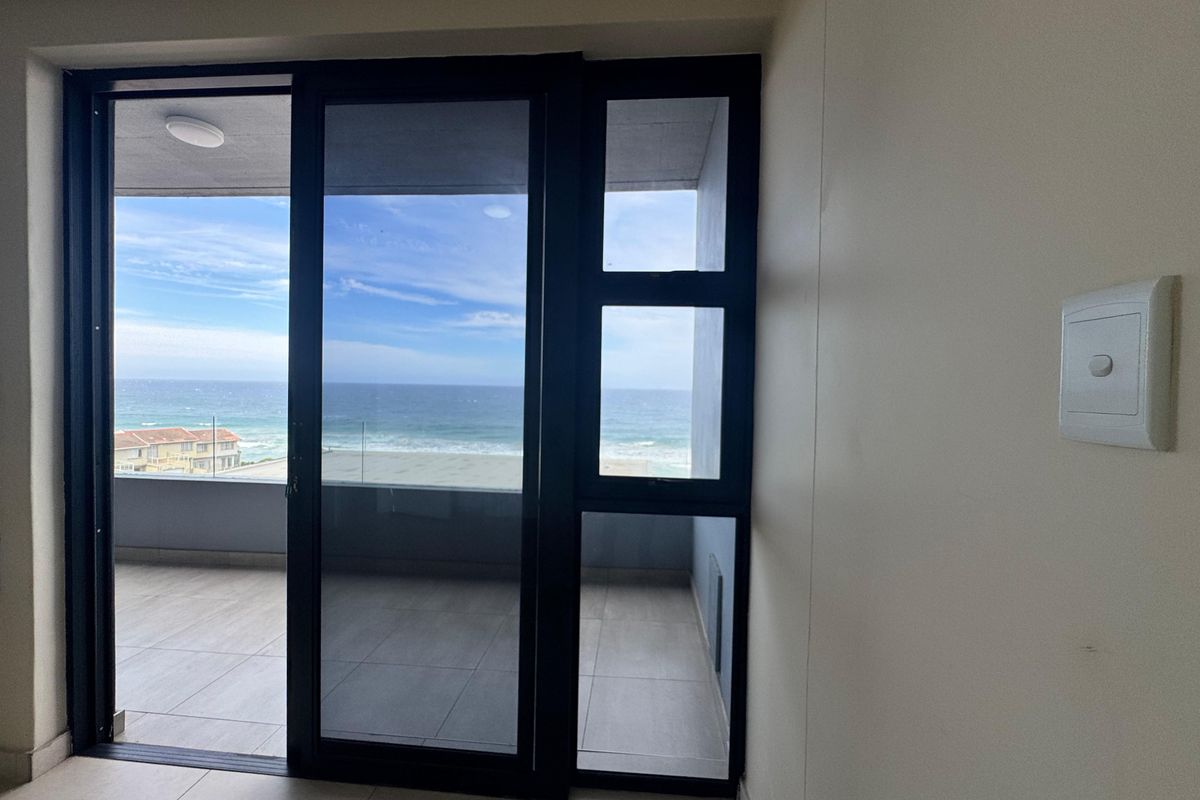 Bright living area featuring large sliding glass doors that open onto a balcony with scenic ocean views.
