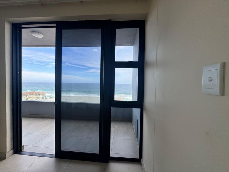 Bright living area featuring large sliding glass doors that open onto a balcony with scenic ocean views.
