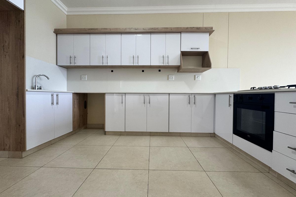A modern, clean kitchen featuring white cabinetry with wood-tone accents, built-in oven, gas hob, and neutral tiled flooring in an open-plan layout.