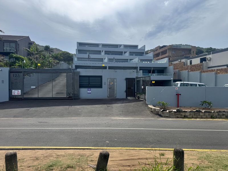 Front elevation of a modern multi-level apartment complex featuring secure gated access, perimeter walling with electric fencing, and paved driveway.