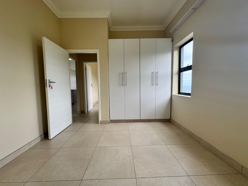 A bright, empty bedroom featuring neutral tiled flooring, built-in white cupboards, and classic ceiling cornicing, offering a clean canvas for personalization.