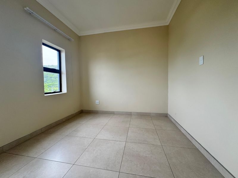 A clean, empty bedroom featuring neutral tiled flooring, coved ceilings, and a window providing natural light.