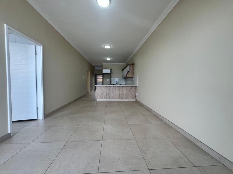 Spacious open-plan living area featuring neutral tiled flooring, recessed lighting, and a modern kitchen with built-in cabinetry and a functional island.