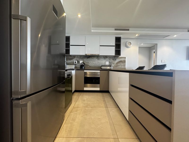 Modern kitchen featuring sleek gloss cabinetry, stone countertops, integrated appliances, and high-quality tiled flooring with recessed ceiling lighting.