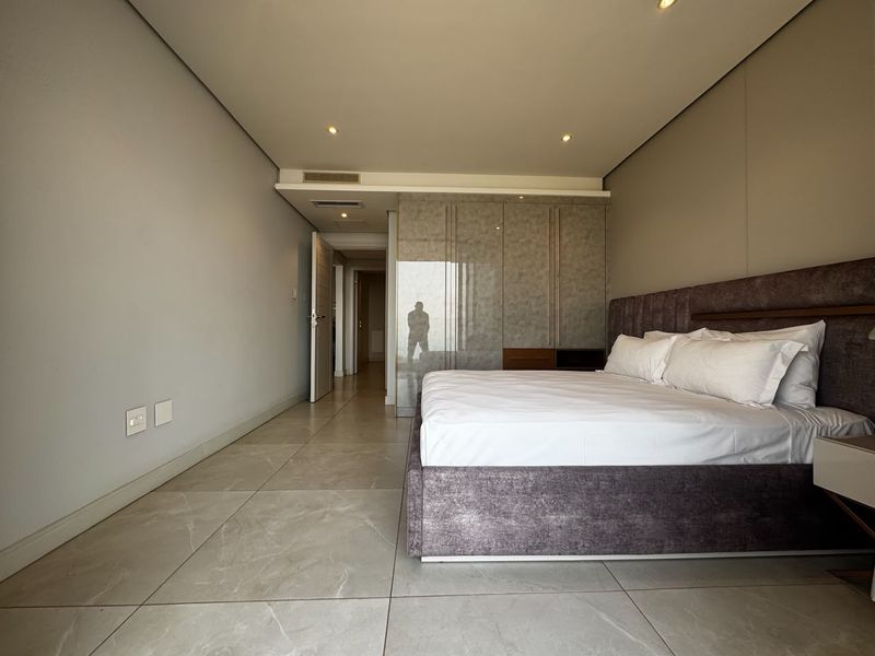Modern bedroom featuring large-format tiled flooring, recessed ceiling lighting, ducted air conditioning, and sleek built-in wardrobes with a reflective finish.