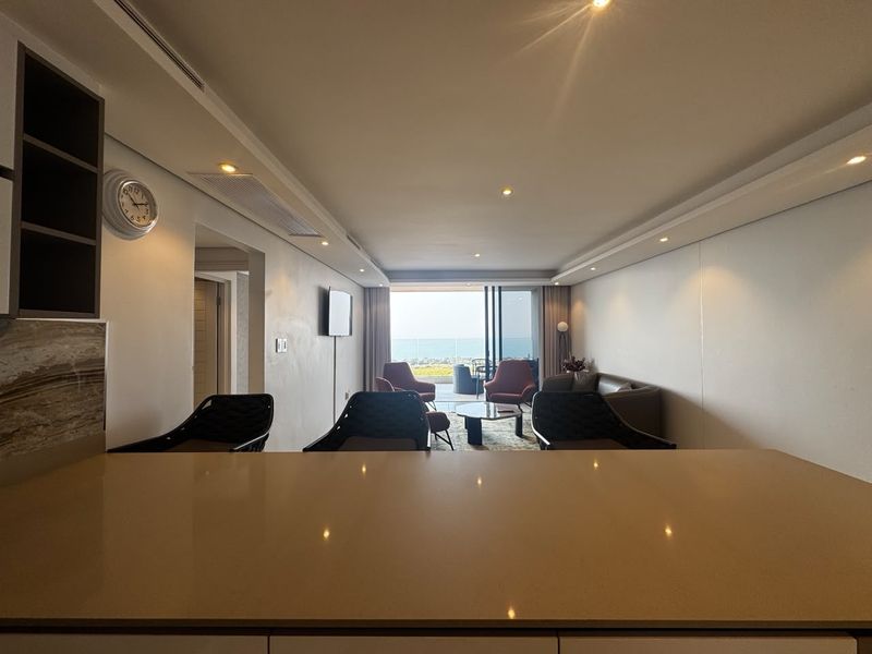 Modern open-plan living area featuring a stone kitchen island, recessed lighting, and seamless access to a balcony with ocean views.