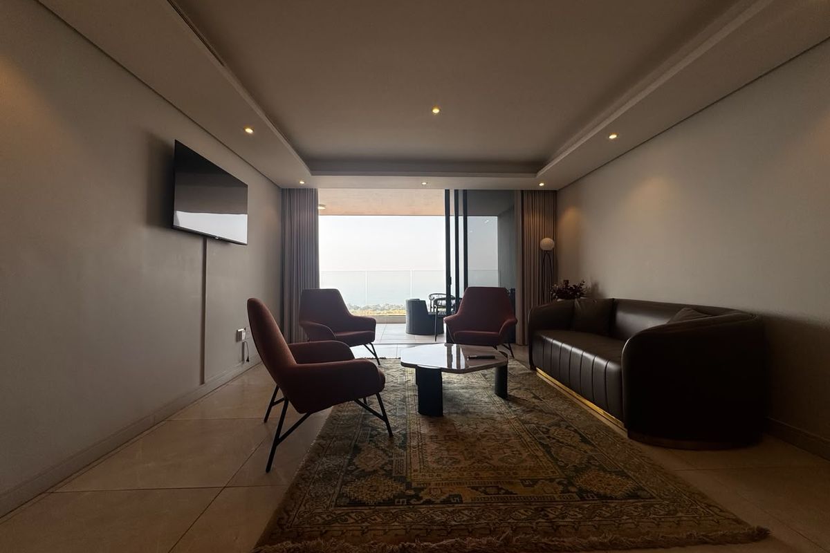 A modern living room featuring tiled floors, recessed ceiling lighting, and large sliding glass doors that open onto a balcony with outdoor views.