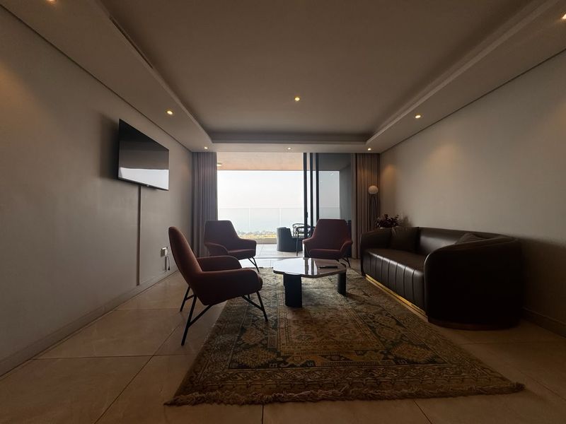 A modern living room featuring tiled floors, recessed ceiling lighting, and large sliding glass doors that open onto a balcony with outdoor views.