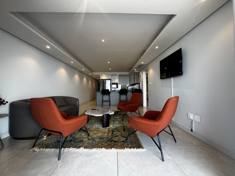 Modern open-plan living area featuring tiled floors, recessed ceiling lighting, and a functional kitchen island, creating a seamless flow between kitchen and lounge spaces.