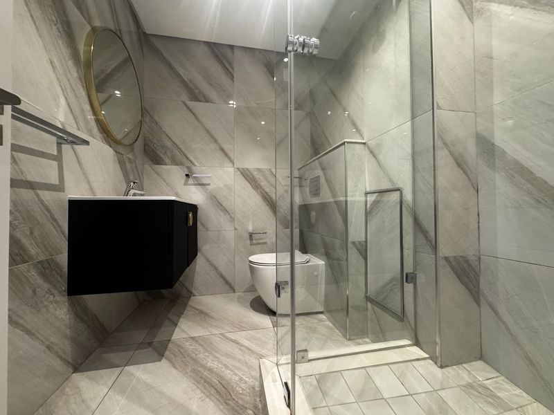 Modern bathroom featuring large-format marble-look tiles, a wall-mounted vanity, a wall-hung toilet, and a sleek glass-enclosed shower.