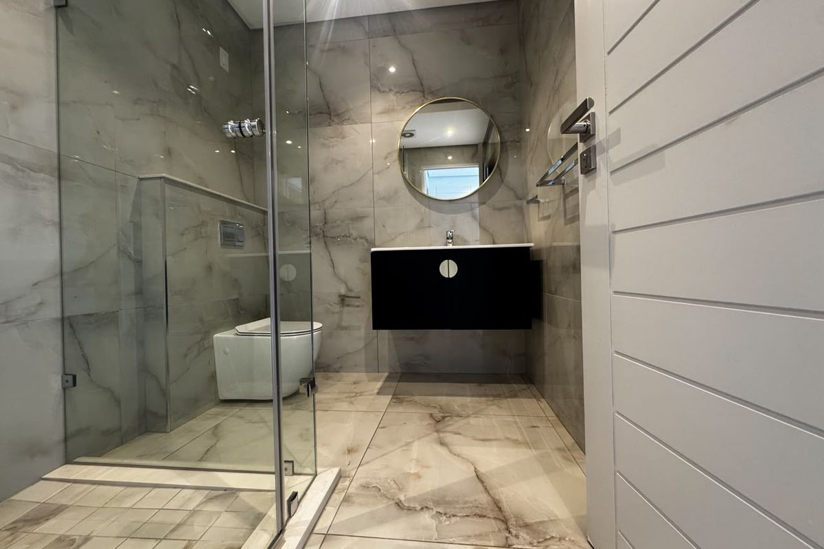 Modern bathroom featuring marble-look floor and wall tiles, a walk-in glass shower, wall-hung vanity, and a wall-hung toilet with a concealed cistern.