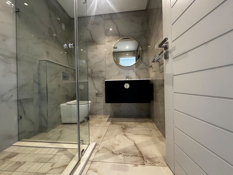 Modern bathroom featuring marble-look floor and wall tiles, a walk-in glass shower, wall-hung vanity, and a wall-hung toilet with a concealed cistern.