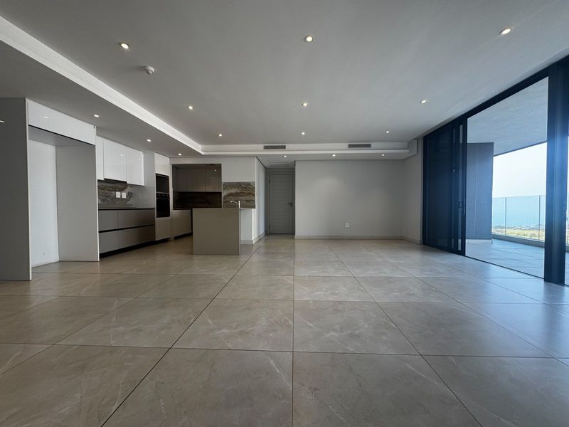 Spacious open-plan living and kitchen area featuring modern cabinetry, large format floor tiles, and seamless access to a private balcony with scenic views.