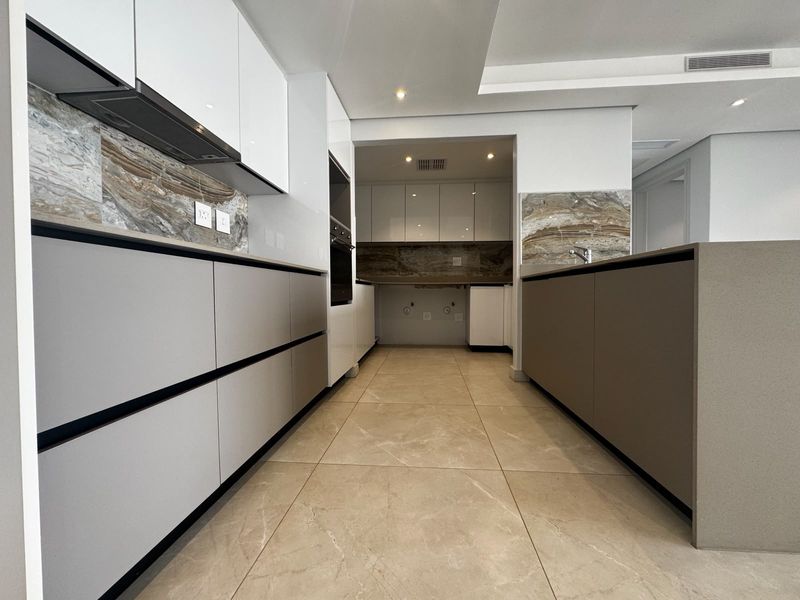 Modern kitchen featuring sleek handleless cabinetry, stone splashbacks, integrated appliances, and high-quality tiled flooring in a clean, contemporary layout.